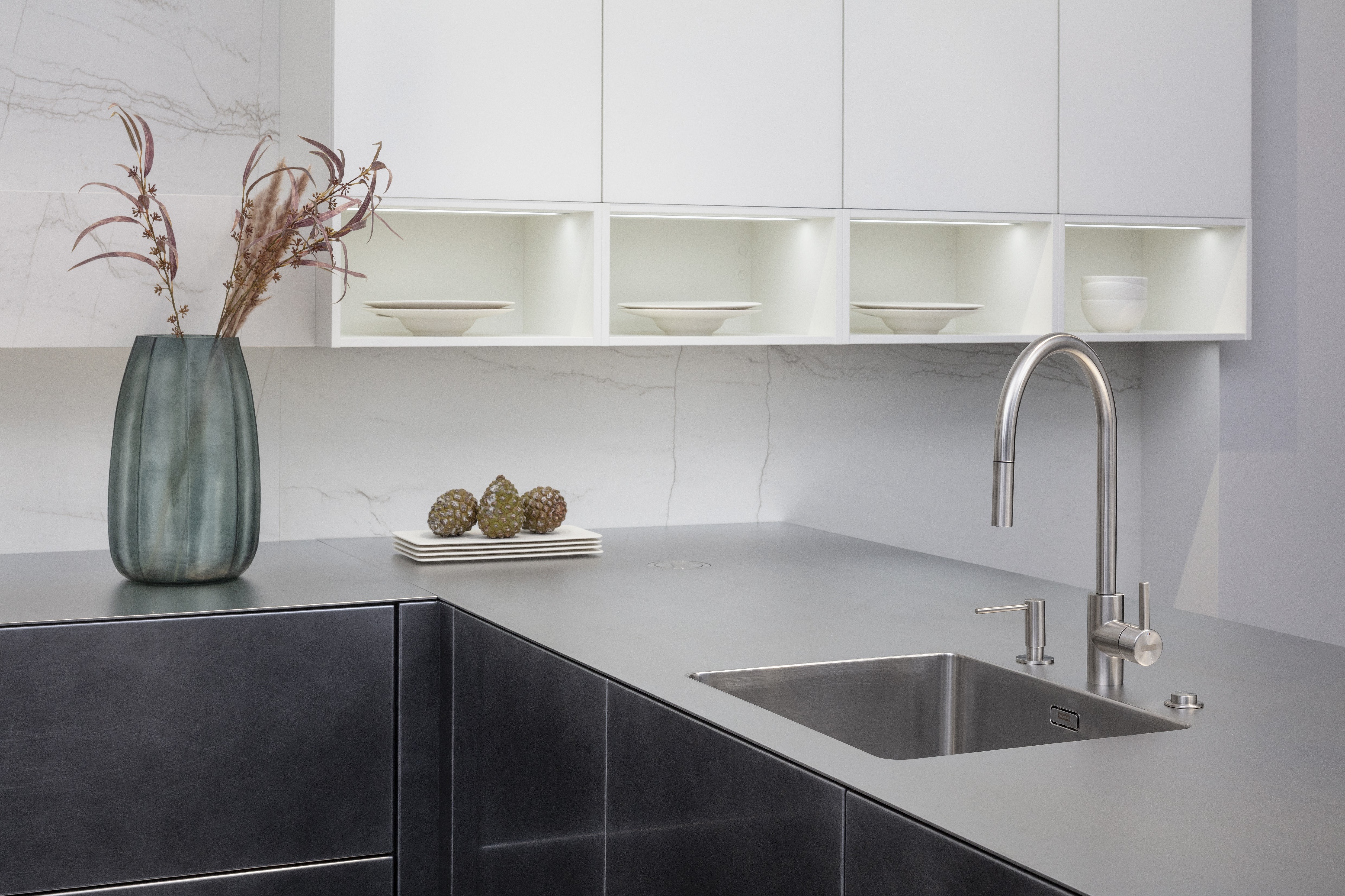 Front: Industriestahl Metalliclack geschliffen AV6000 NCS Mattlack APL: Franke Edelstahl 6 mm Geräte: Bora Spüle Armaturen: Franke  Features: Metallfront, Spülbecken in APL integriert (aus einem Guss), Oberschränke mit Lowboard-Charakter, integrierter Arbeitsplatz, dunkler Korpus mit Aluminium-Abschlussleiste, Wärmeschublade mit Gittereinsatz.