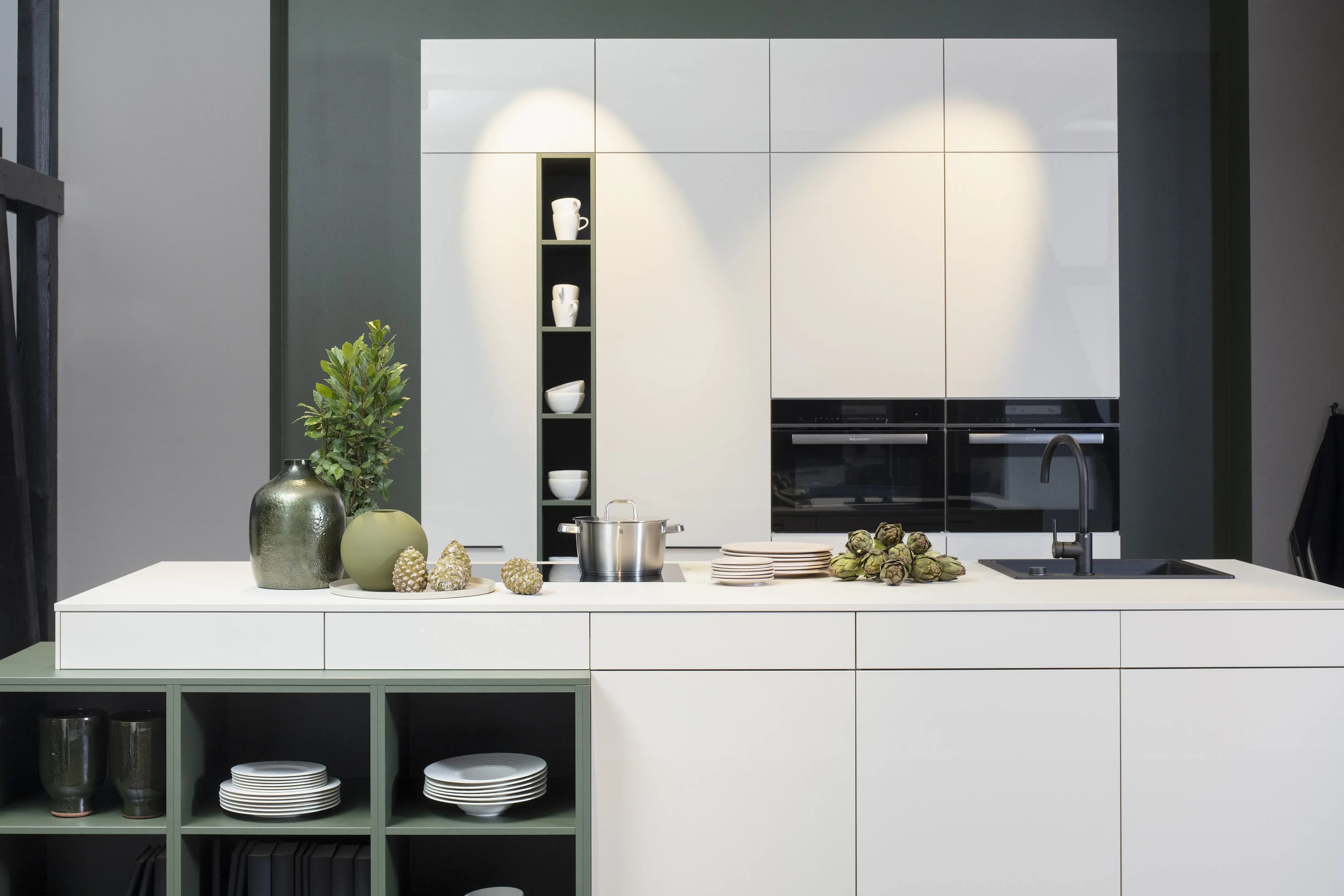 Concept130 Front: Perfect Sense Perfect Brillant Crema magnolia UV Hochglanz lackiert Front 2: Perfect Sense Scala Olivgrün Grüne Front? APL: Perfect Sense Crema Magnolia 16 mm Griff: Schwarz Metall matt Geräte: Blaupunkt Spüle und Armatur: Franke  Features: offene Regale in zweiter Frontfarbe abgesetzt, Apothekerschrank, Spüle in Schwarz.